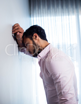 Side view of thoughtful young businessman standing against wall