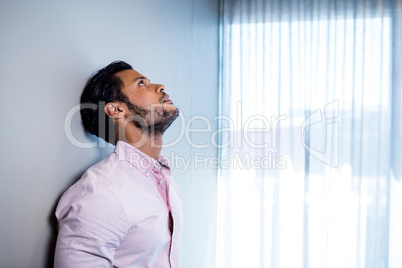 Businessman standing against wall and looking up Businessman standing against wall and looking up
