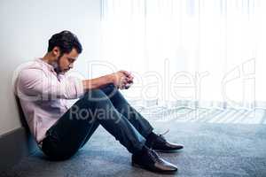 Depressed businessman sitting against a wall and looking down