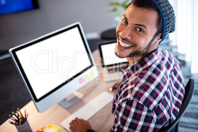 Smiling hipster man posing for camera while sitting at computer