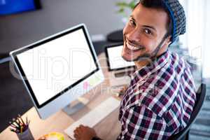 Smiling hipster man posing for camera while sitting at computer