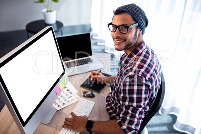 Smiling hipster man posing for camera while sitting at computer