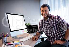Smiling hipster man posing for camera at computer desk in studio