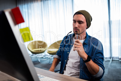 Hipster man holding glasses while working at computer desk