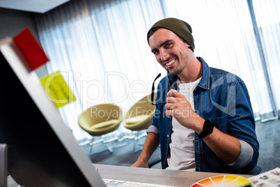 Hipster man holding glasses while working at computer desk