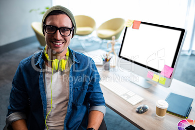Smiling hipster businessman posing for camera while sitting at d