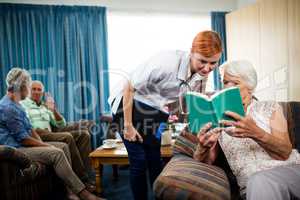 Senior woman reading book with nurse