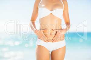 Mid section of woman in bikini touching her belly