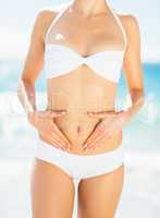 Mid section of woman in bikini touching her belly