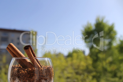 cinnamon sticks in a glass of wine with granulated coffee, left on the background of the city