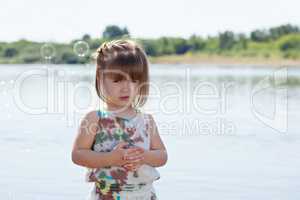 Cute little girl posing with soap bubbles at lake