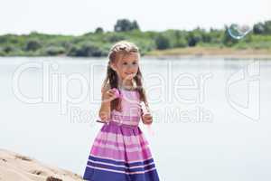 Beautiful little girl blowing soap bubbles in park
