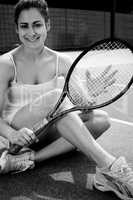 Pretty tennis player sitting on court smiling at camera