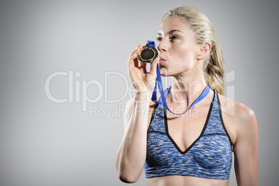 Composite image of happy female athlete kissing medal