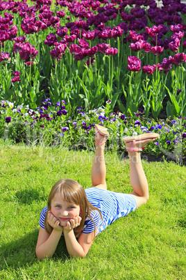 little girl lies on the grass near the tulips