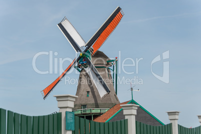 Mühle mit bunten Flügeln vor grünem Zaun