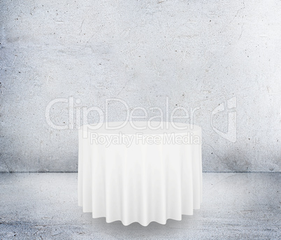 Empty round table with tablecloth isolated on concrete background