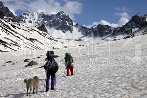 Two hikers with dog in spring snowy mountains