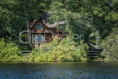 Brown thatched villa in trees on riverbank