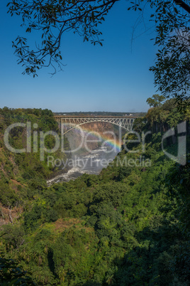 Rainbow spanning canyon beneath Victoria Falls Bridge