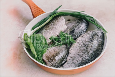 Fish and components for her preparation in a large skillet.