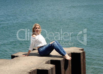 Pretty girl sitting on pier on lake.