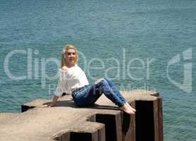Pretty girl sitting on pier on lake.