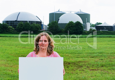 Frau hält ein Schild vor Biogasanlage