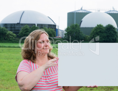 Frau hält ein Schild vor Biogasanlage