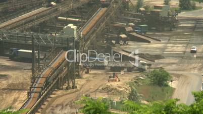 Open-cast mining. Trucks driving under flat conveyor terminal. Medium shot. Surface mine.