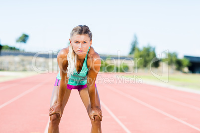 Tired female athlete standing on running track