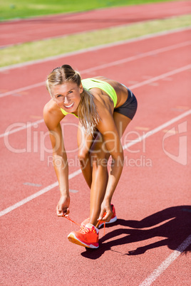 Portrait of female athlete tying her shoe laces on running track