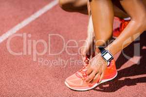 Female athlete tying her shoe laces on running track