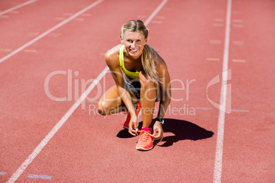 Portrait of female athlete tying her shoe laces on running track