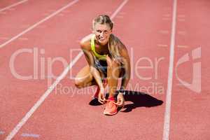 Portrait of female athlete tying her shoe laces on running track