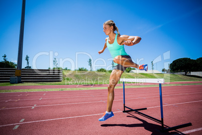 Female athlete jumping above the hurdle