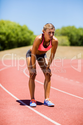 Tired female athlete standing on running track