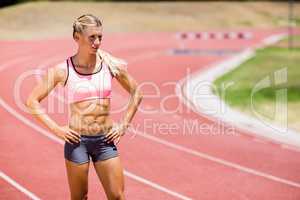 Female athlete standing with hand on hips on the running track