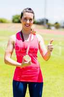 Portrait of female athlete showing gold medal with thumbs up