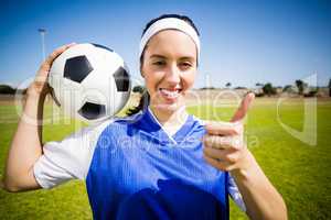 Happy soccer player holding a ball and showing her thumbs up