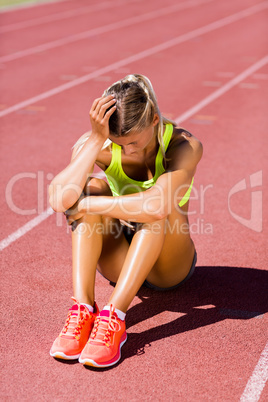 Upset female athlete sitting on running track