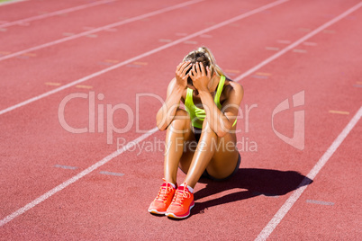 Upset female athlete sitting on running track