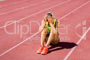 Upset female athlete sitting on running track