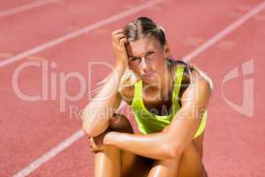 Upset female athlete sitting on running track