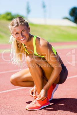 Portrait of female athlete tying her shoe laces on running track