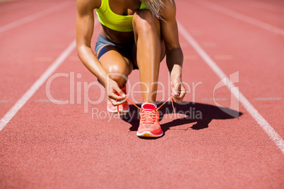Female athlete tying her shoe laces on running track