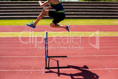 Female athlete jumping above the hurdle