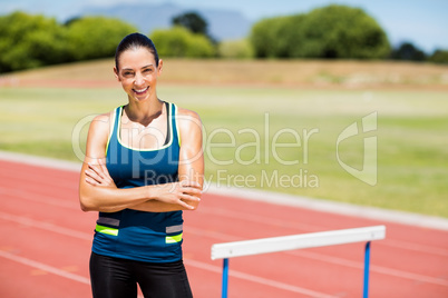 Portrait of female athlete standing beside hurdle