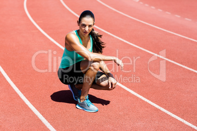 Portrait of female athlete kneeling on running track