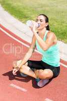 Tired female athlete sitting on the running track and drinking w